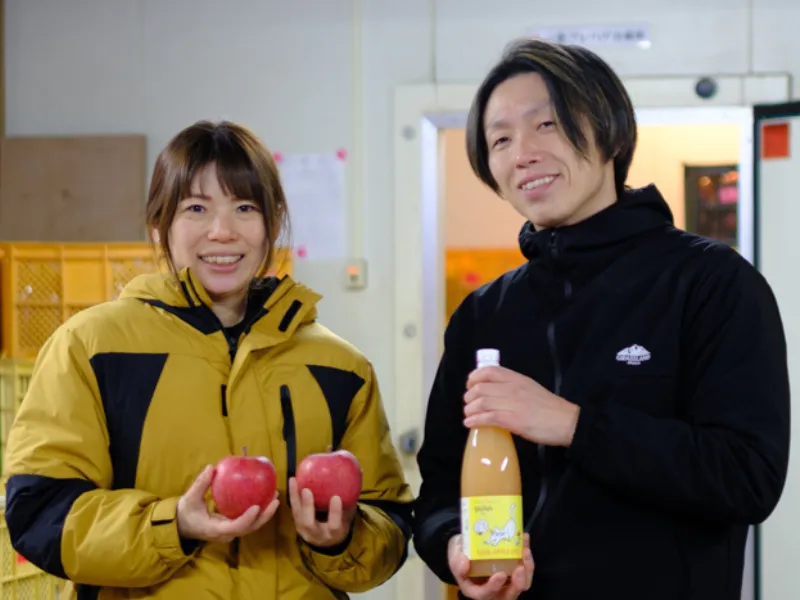 Couple holding apples and smiling in an orchard